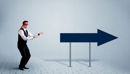 A lost young sales person with blindfolds trying to find the right path concept with large blue arrow sign pointing forward.