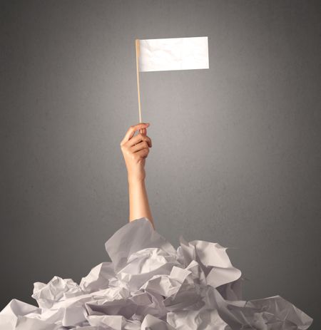 Female hand emerging from crumpled paper pile holding a white blank flag 