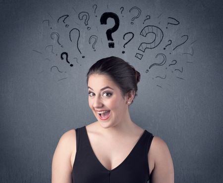 A pretty teenage girl standing confused in front of grey wall background with drawn question marks concept.