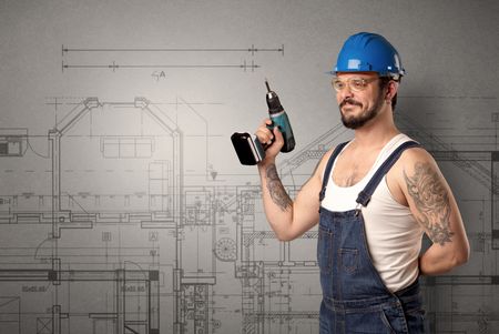 Worker standing with tool in his hand in front of technical drawings.