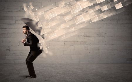 Business man protecting with umbrella against wind of papers concept