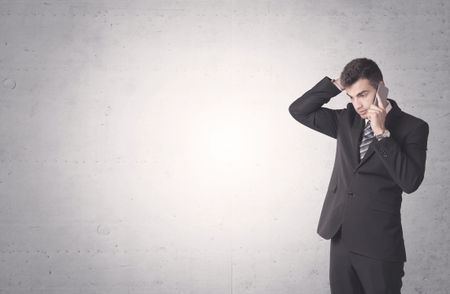 Young sales business person in elegant suit standing in front of clear empty grey wall background while talking on the phone