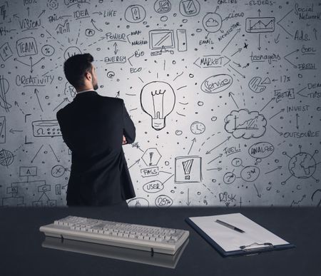 An intelligent office worker drawing strategy ideas and future plan keywords on wall at a brainstorming meeting in office concept