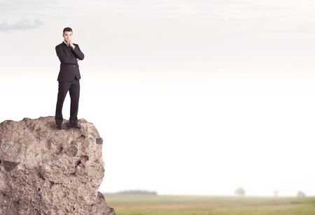 A successful good looking business person standing on top of a high cliff above country landscape with clear white sky concept