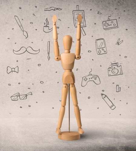 Wooden mannequin posed in front of a greyish background with hobby related scribbles behind it