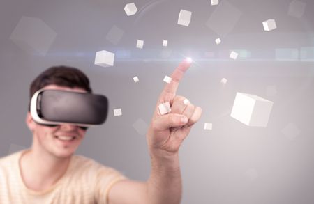 Young impressed man wearing virtual reality goggles with grey cubes around him 