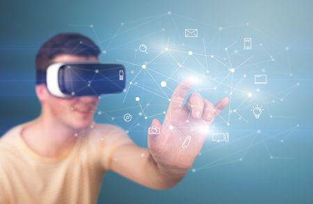 Young impressed man wearing virtual reality goggles with mixed media icons around his finger