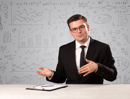 Young handsome businessman sitting at a desk with white charts behind him