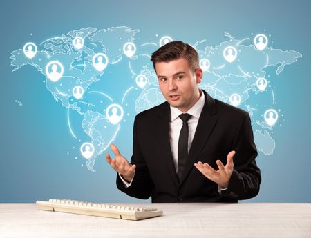 Young handsome businessman sitting at a desk with a blue world map behind him