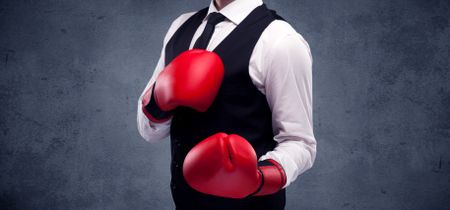 A well dressed sales person standing with red boxing gloves on his hand in front of urban grey wall background concept.