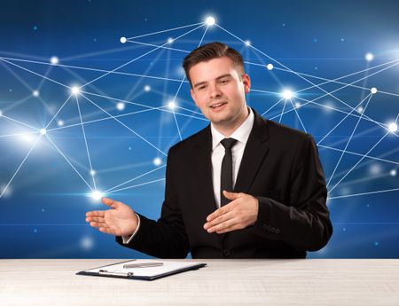 Young handsome businessman sitting at a desk with a blue connection graphic behnid him