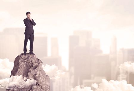 A professional winner business person standing on a dangerous mountain top above the city scape with clouds concept