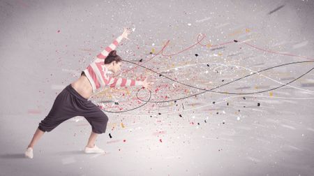 A young contemporary energetic dancer in action in front of a grey wall background with lines, spray dots and splatter concept