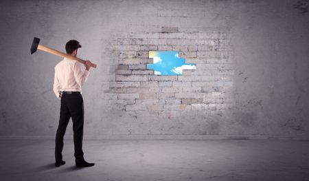 Business man hitting grungy brick wall with hammer