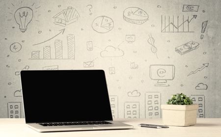 An open laptop on a white office desk with flower, coffee, books in front of wall background full of financial business charts concept