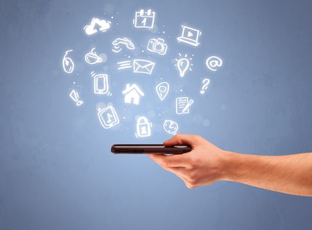 An elegant caucasian white hand holding mobile phone with drawn social media icons in front of an empty clear blue background concept