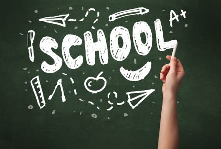 A teacher writing school, drawing children things on clean green chalkboard by hand