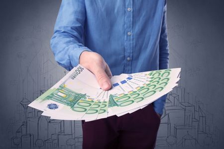 Young businessman holding large amount of bills with grungy drawings of a city and numbers behind him