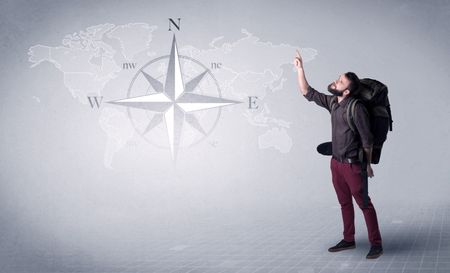 Handsome young man standing with a backpack on his back and a compass and a world map in the background