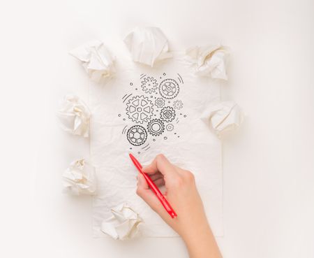 Female hand next to a few crumpled paper balls drawing rotating gears