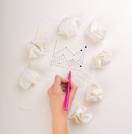 Female hand next to a few crumpled paper balls drawing a progress chart