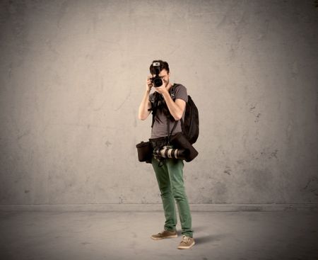 A professional male photographer with belt holding a camera and taking photos in front of clear grey urban wall background concept