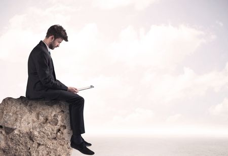 A young sales person in elegant suit sitting with paper on top of a stone in the clouds concept