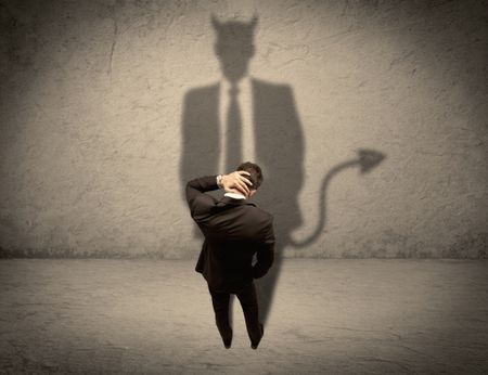 An experienced tricky businessman in suit looking at his devil desguise shadow reflected on the wall concept