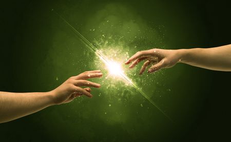 Two naked male hands about to touch, lighting the spark with modest explosion in front of green background concept