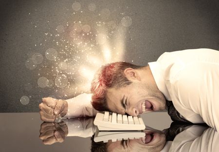 A young depressed business person laying his head on computer keyboard with thoughts exploding from his head illustrated by light beams concept