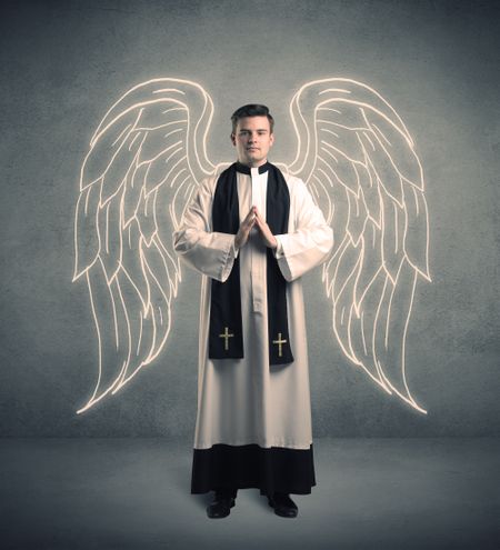A young male priest with drawn large angel wings standing with the holy bible in his hands concept.