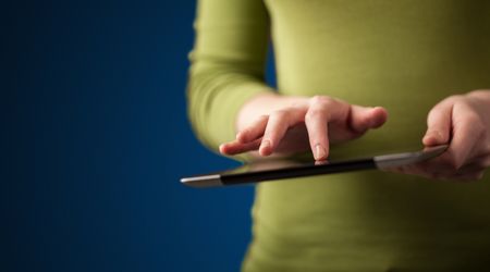 Close up of hand holding digital touchpad tablet device on background