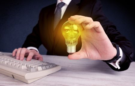 A business man in suit holding a glowing yellow light bulb in his hand while working in the office concept.