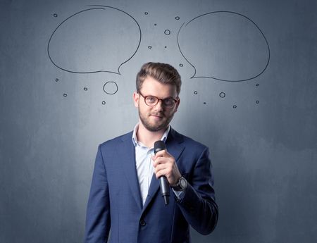 Businessman speaking into microphone with speech bubbles over his head