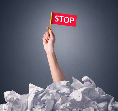 Female hand emerging from crumpled paper pile holding a red flag with stop written on it 