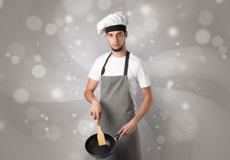 Male cook with kitchen tools and shiny grey wallpaper
