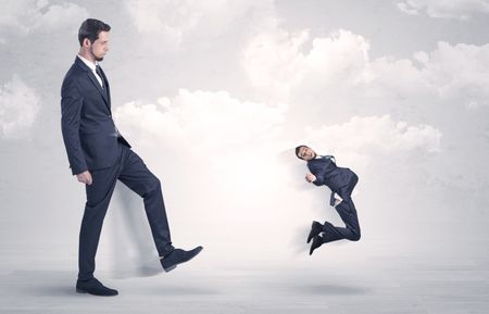 Big businessmen kicking himself as a small employee with cloudy background