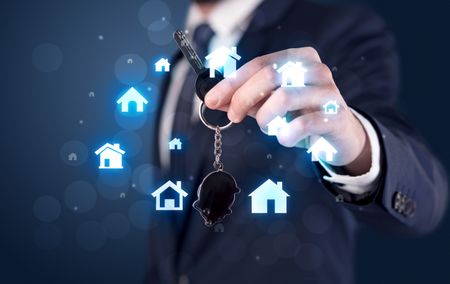 Businessman in suit holding keys with house graphics around and dark background
