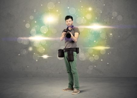 A young amateur photographer with professional camera equipment taking picture in front of grey wall full of colorful bokeh and glowing lights concept