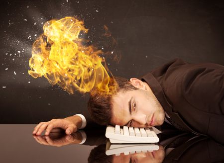 A depressed businessman banging his head in a keyboard and shouting with his head on fire, reflecting on desk