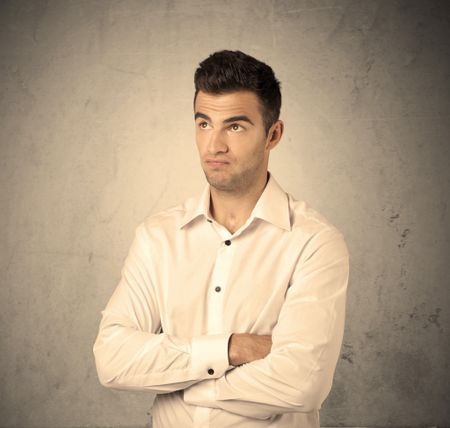 A young handsome business person making facial expression in front of clear, empty concrete wall background concept