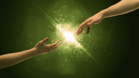 Two naked male hands about to touch, lighting the spark with modest explosion in front of green background concept
