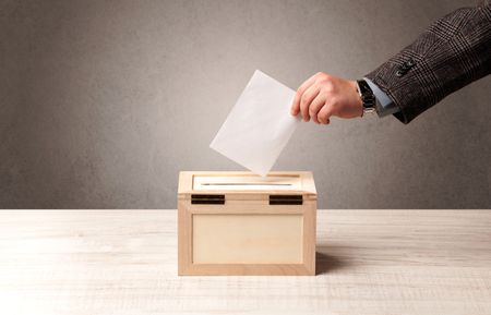 Ballot box with person casting vote on blank voting slip, grungy background