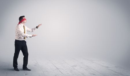 A young male business person in elegant dress standing with red blindfolds in a clear, empty space concept.