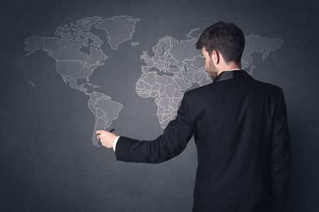 Young businessman in black suit standing in front of a black world map 