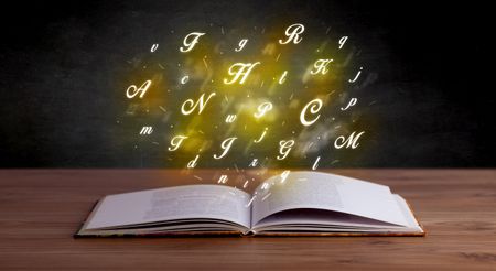 Glowing yellow alphabet letters coming out of an open book 