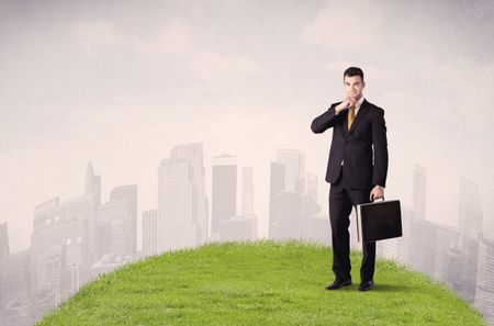 A confident male well looking office manager standing in small green grass in front of city landscape with tall buildings concept.