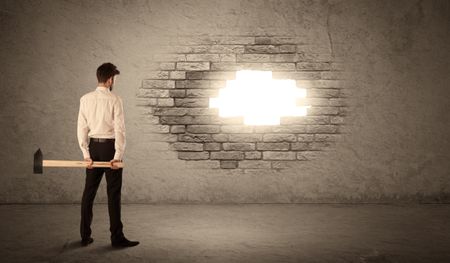 Business man hitting brick grungy wall with hammer and opening a hole