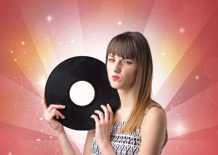 Young lady holding vinyl record on a red background with lights shining behind her