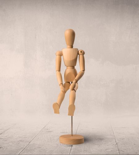 Wooden mannequin posed in front of a greyish background